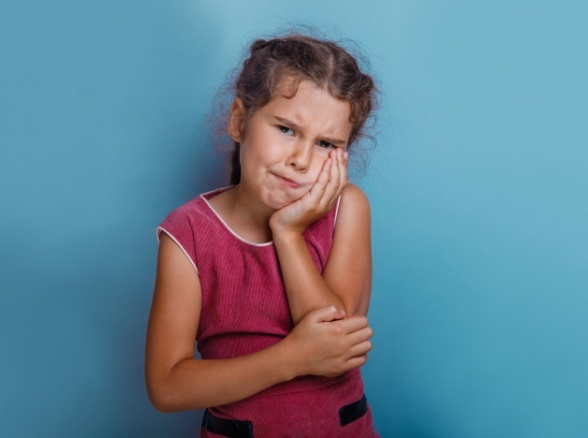 Child holding cheek in pain before emergency dentistry