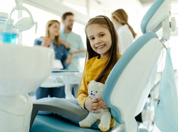 Child smiling with stuffed animal while dentist and parents talk