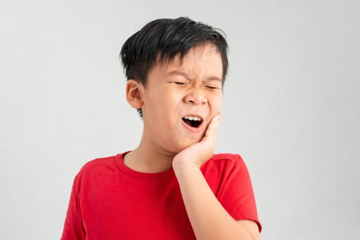 Little boy in red shirt pressing hand to jaw in pain