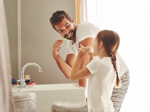 Father and daughter smiling while brushing their teeth in bathroom