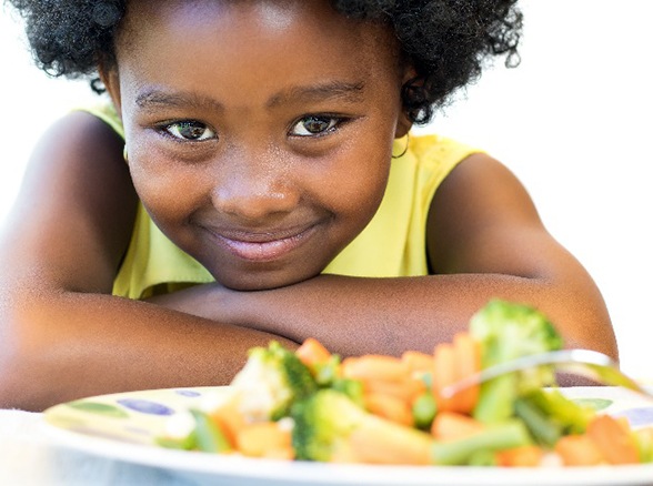 Child smiling with plate of healthy food in front of her