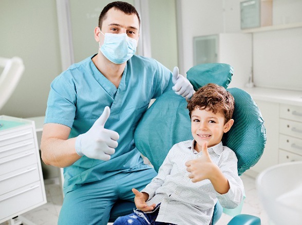 Pediatric dentist and child smiling while giving thumbs up