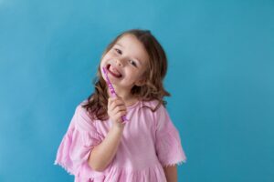 Girl in pink shirt holding purple toothbrush and smiling