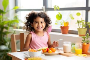Little girl in a pink shirt eating vegetables at a table with plants